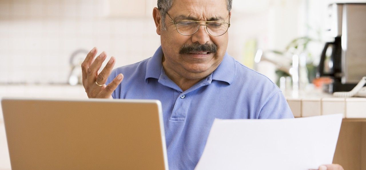 man-in-kitchen-with-laptop-and-paperwork-frustrated-SBI-301052643